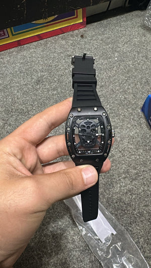 "Tonneau-style black metal watch featuring skeleton skull dial and sport design"
